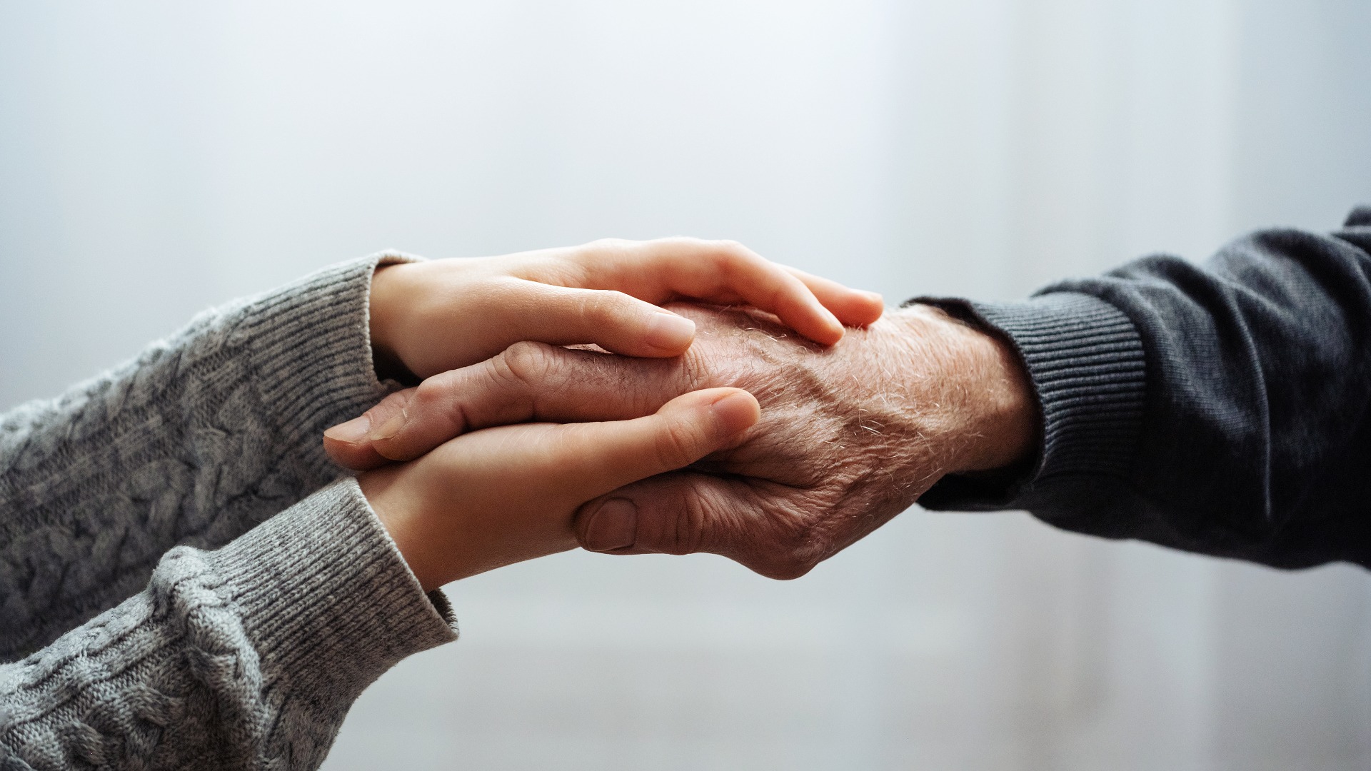 Closeup of hands of old man and a young female hands. Senior man, with caregiver indoors. Helping hand for the elderly concept with young hand holding old hand.