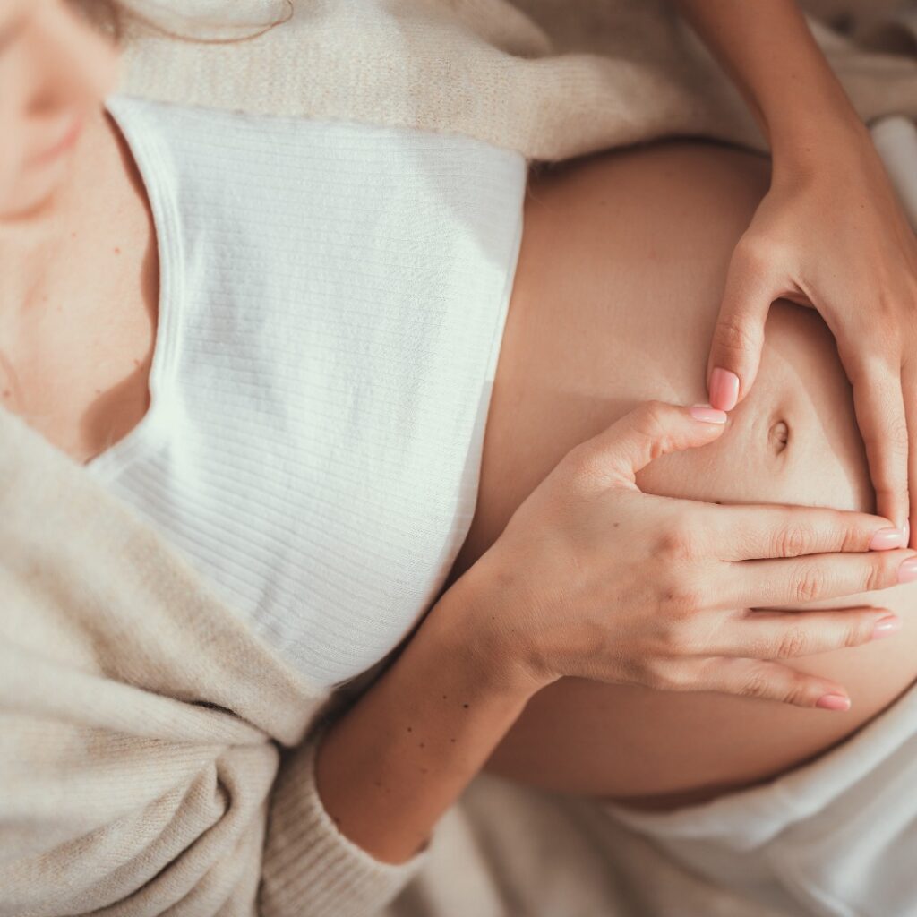 Hübsche Mutter macht Herzform mit Händen über dem Bauch