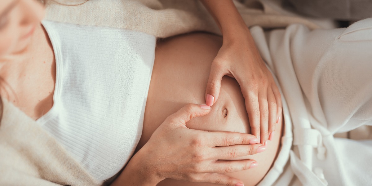 Hübsche Mutter macht Herzform mit Händen über dem Bauch