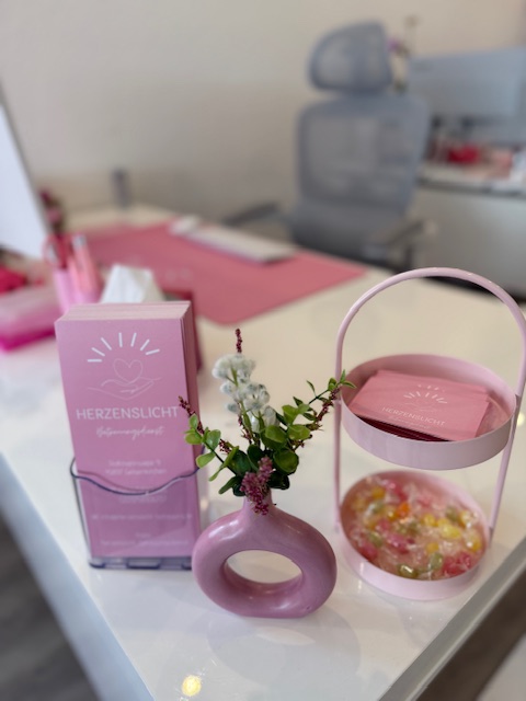 Rosa Schachtel und Vase mit Blumen auf Tisch, daneben runder Behälter mit Bonbons, moderne Einrichtung.